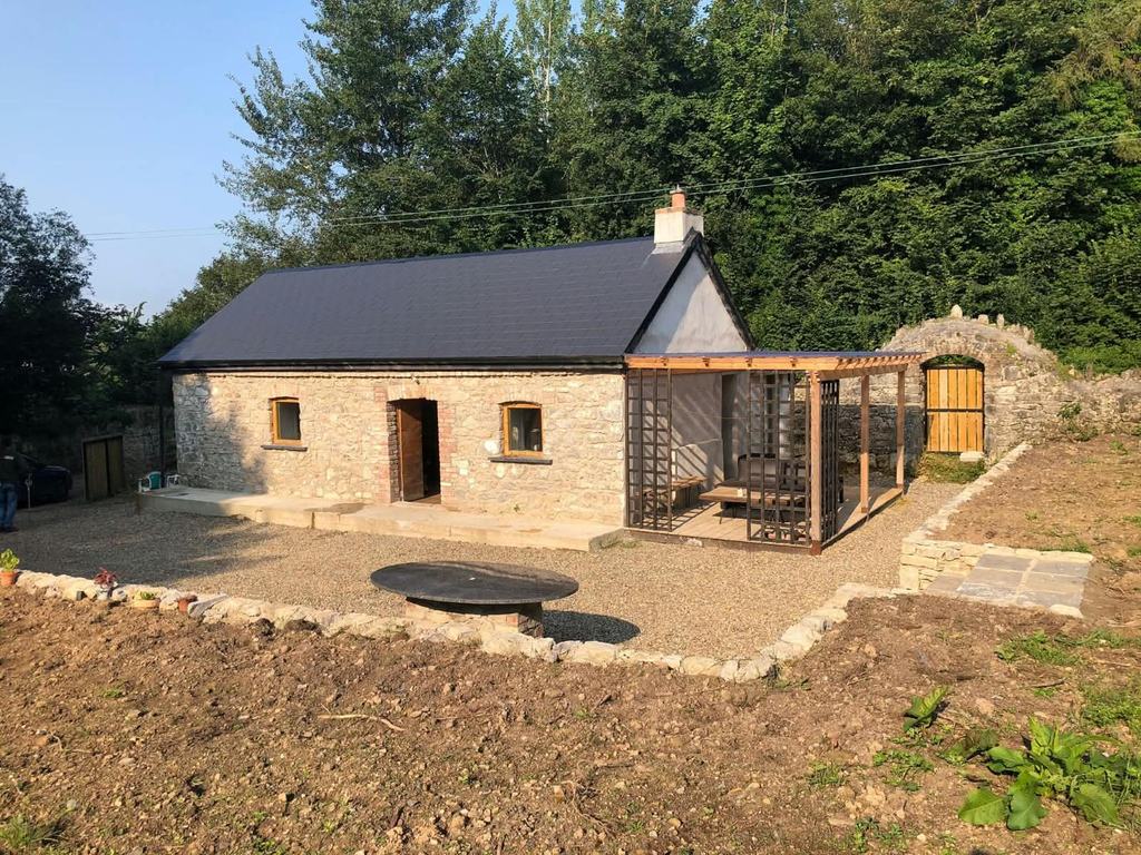 Restored stone barn with a new slate roof, brick window reveals and an oak-framed canopy over a timber deck.